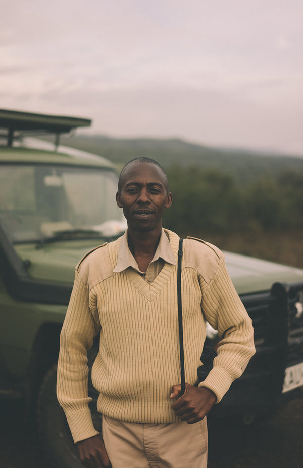 A ranger, posing with binoculars swung over shoulder and a 4WD in the background.