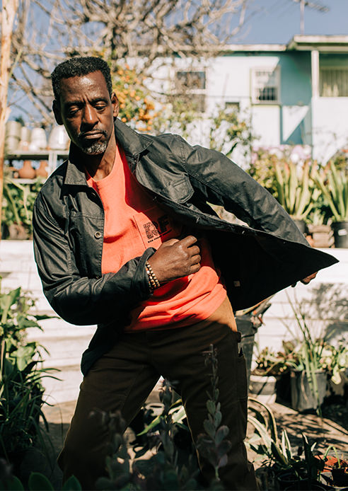 Ron dancing in his garden while wearing The Heavy Bag Tee in Hibiscus and The Carpenter Pant in Cedar Boss Duck.