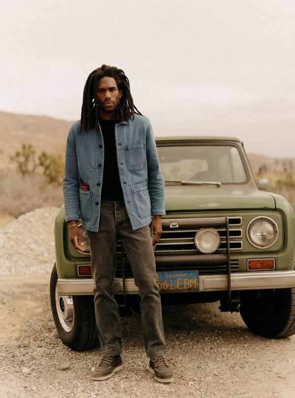 Model standing in front of a vintage green jeep, wearing The Primer Jacket in Washed Indigo Terry