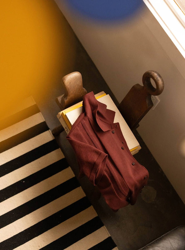 The Button Polo in Dried Cherry Stripe, draped over a stack of books