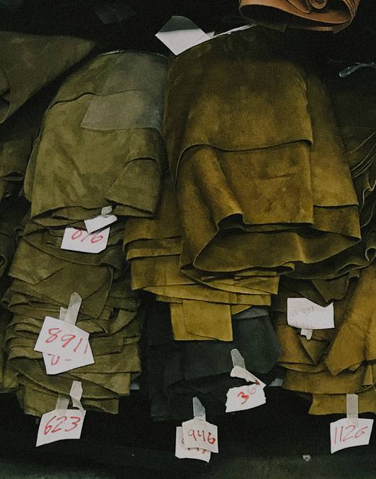 Stacks of olive green fabrics are arranged and labeled with white notecards bearing handwritten red numbers.