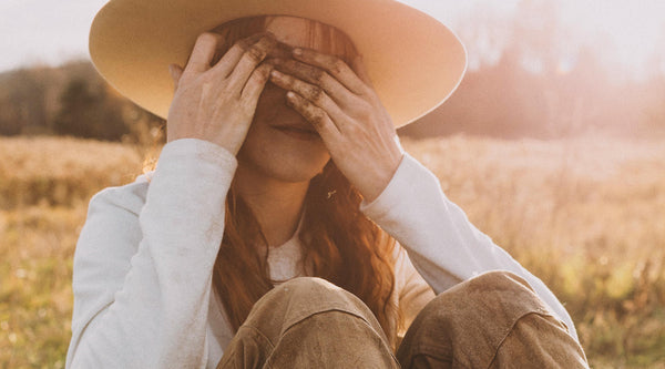 Kate sitting in a sunny field, covering her eyes.